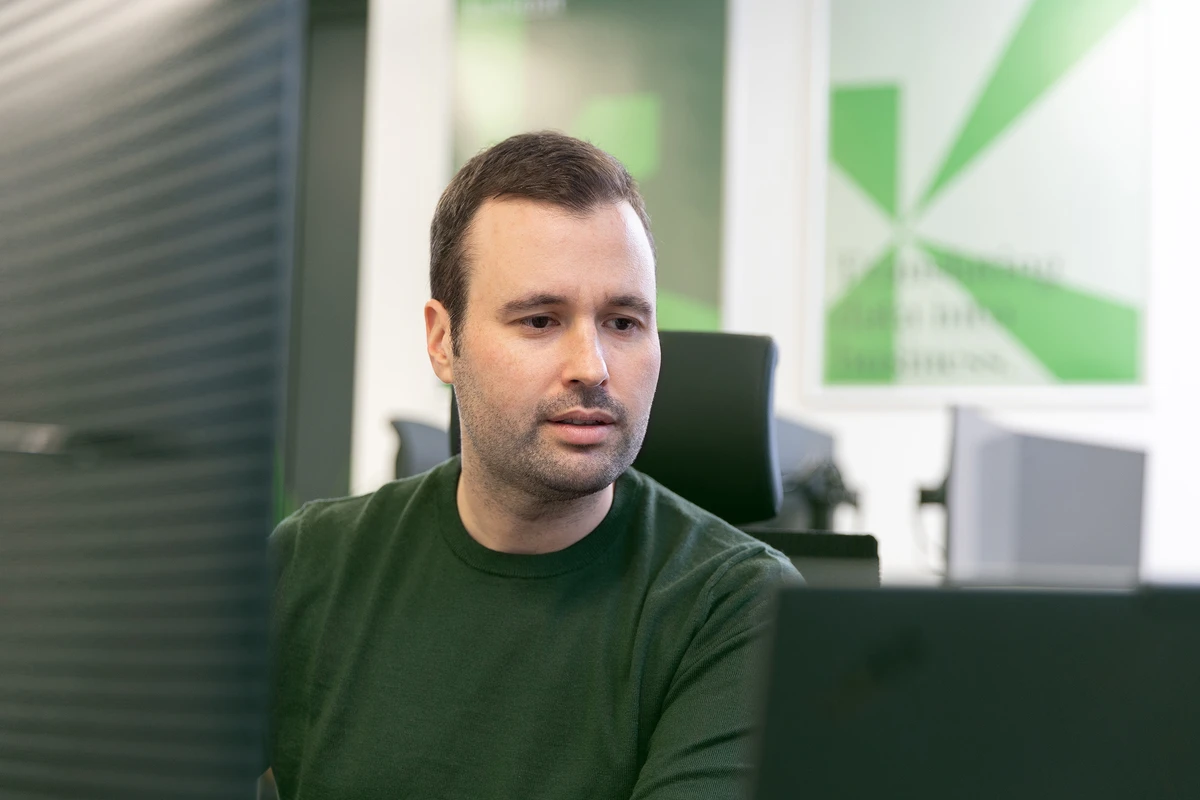 Person sitzt an einem Schreibtisch und blickt auf einen Monitor.