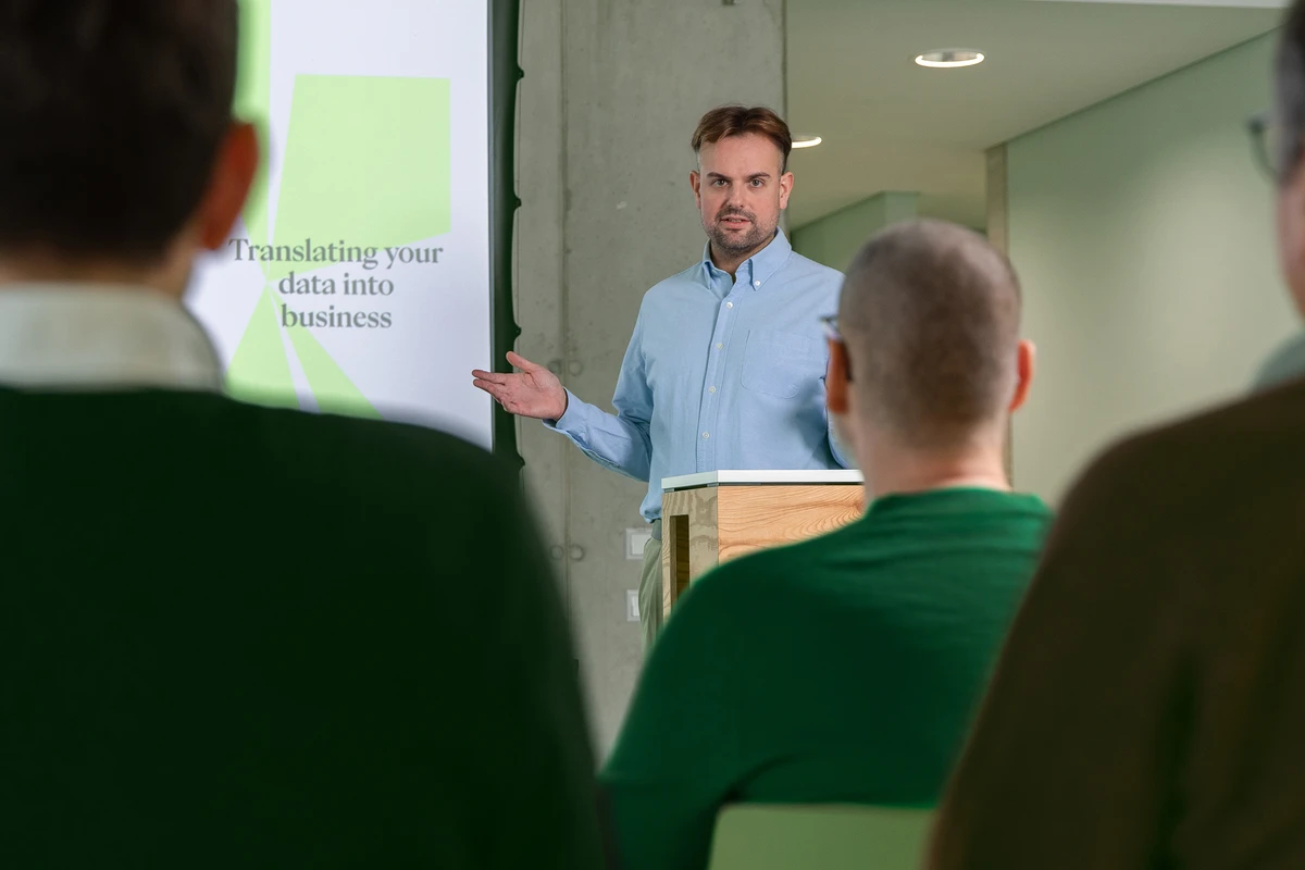 Daten in Business-Wert verwandeln mit Data Consulting. Person steht an einem Rednerpult und spricht vor einer sitzenden Gruppe.
