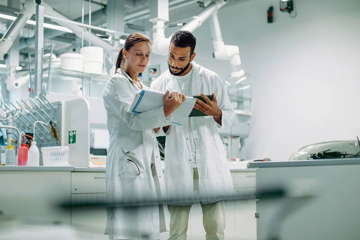 Zwei Mitarbeitende besprechen Laborergebnisse anhand eines Tablets und einer Dokumentation in einem Labor.