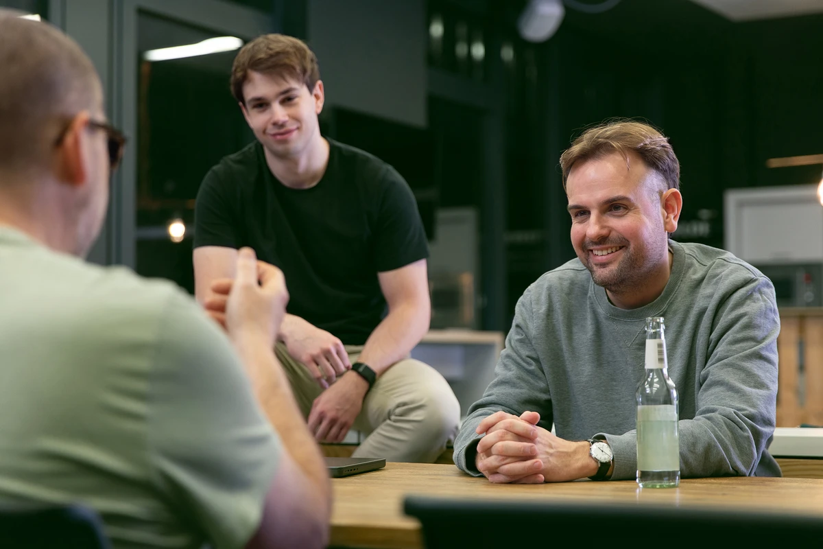 Lockere Atmosphäre in der Küche, drei Personen führen ein Gespräch.